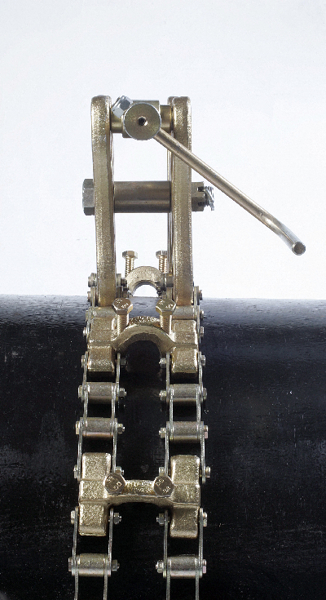 A close-up view of a metal chain tensioner mechanism mounted on a black cylindrical surface, with a lever arm extending to the right.